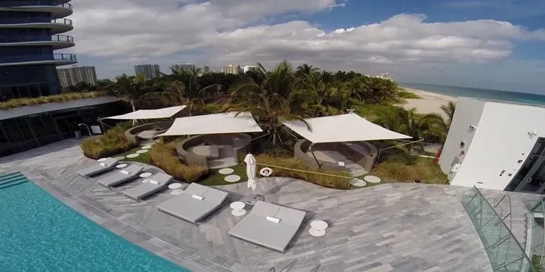Luxurious beachfront poolside with cabanas and trees.