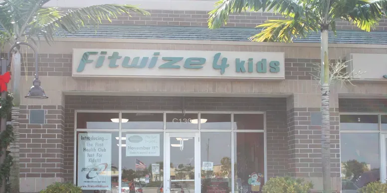 Fitness center storefront with palm trees outside.