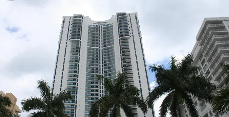 Skyscraper with palm trees and cloudy sky.