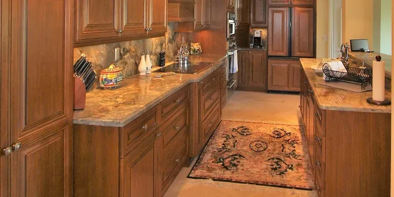 Wooden kitchen with marble countertops and rug.