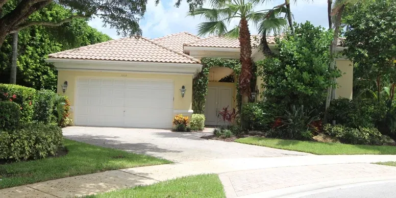 Yellow house with garage and palm trees.